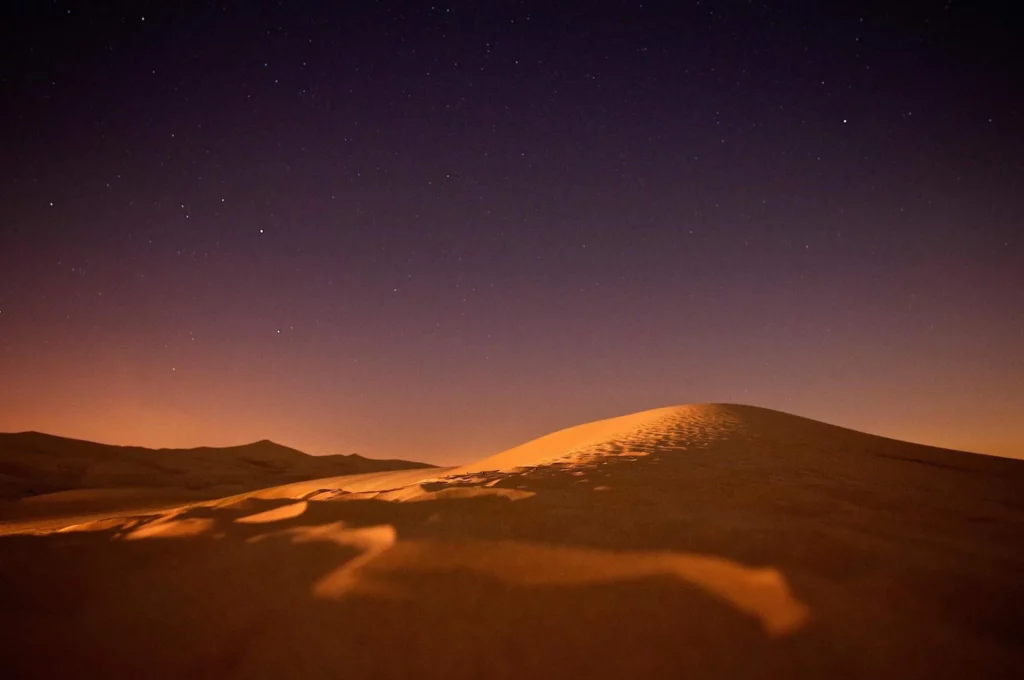 Dunes de sable de désert éclairées sous un ciel nocturne étoilé