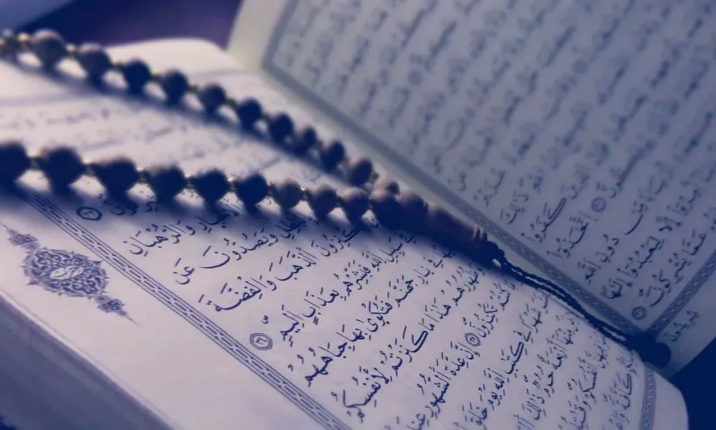 Chapelet de prière posé sur un Coran ouvert aux pages en écriture arabe